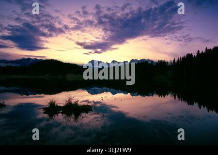 Dramatic glow at dawn before sunrise with romantic colors at a painterly lake with silhouettes of mountains Stock Photo