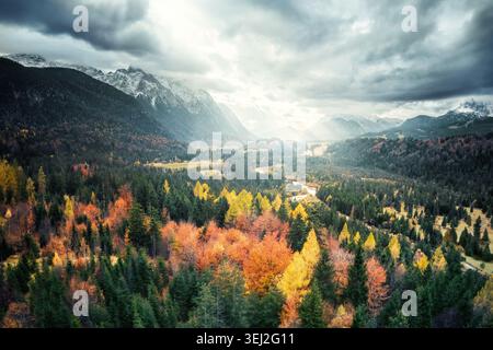 Colorful picturesque autumn forest with dramatic cloudy sky and mountains in the background, aerial landscape view Stock Photo