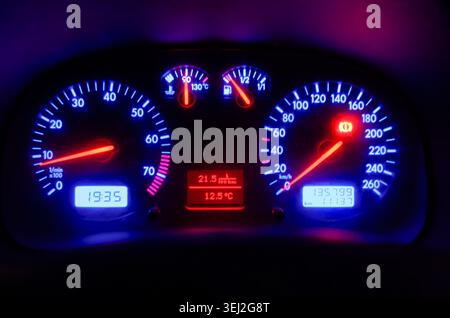 close-up view of a car dashboard at night featuring illuminated blue circular gauges and digital displays showing time, mileage, and temperature in a Stock Photo