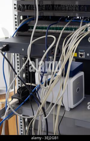 server rack containing network switches and devices with disorganized, tangled white and blue ethernet cables hanging in front Stock Photo