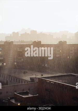 Heavy rain at sunset over residential buildings. Golden hour sunlight cutting through a heavy downpour over apartment buildings and rooftops. Stock Photo