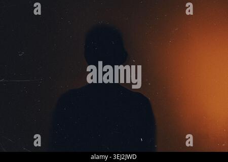 Person silhouette projecting on a dark wall with orange light and film grain effect Stock Photo