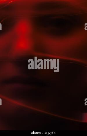 Abstract face blurring with red light and dark shadows evoking mystery and emotion Stock Photo