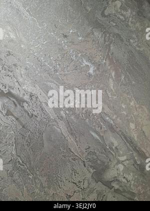 A brushed silver metallic surface displays a wavy texture with reflections. Light hits the surface, creating shiny patterns and variations in depth an Stock Photo
