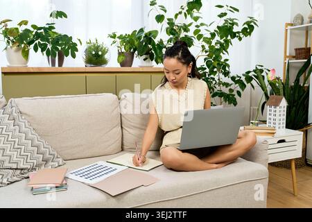 Casual young woman with wavy hair sketches ideas while relaxing in her stylish home. Stock Photo