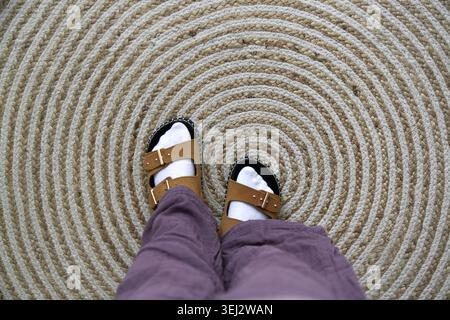 Top view of cream suede children’s sandals worn with white socks on a natural jute rug, cozy boho inspired kids fashion detail with warm earthy tones Stock Photo