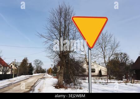 Yield traffic sign on roadside during winter season. Road safety and transportation concept with snowy residential neighborhood. Stock Photo