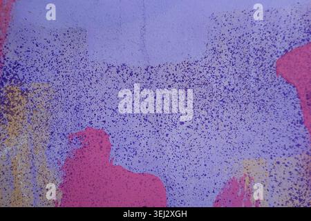 Close-up of urban wall covered with chaotic graffiti paint splashes and spray patterns in vivid purple, pink and blue tones. Stock Photo