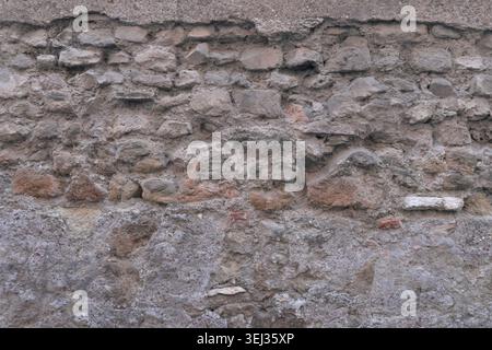 BACKGROUND TEXTURE OF AN URBAN STONE WALL WITH CRACKED PLASTER Stock Photo