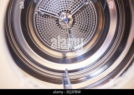 Dryer interior showing clean perforated stainless steel drum ready for clothes. Clean metallic drum inside washing machine for laundry tasks. Stock Photo