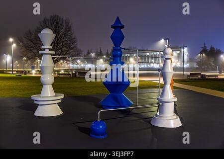 Large decorative chess pieces installation in a public park at night, featuring stylized blue and white figures linked by metal bars under glowing str Stock Photo