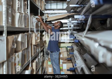 Warehouse worker arranges boxes and checks stocks in an industrial storage site during working hours. Stock Photo