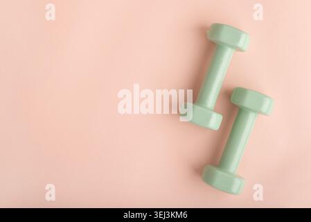 Two light green dumbbells resting on a pink background, symbolizing home workout, exercise, and a commitment to health and well-being Stock Photo