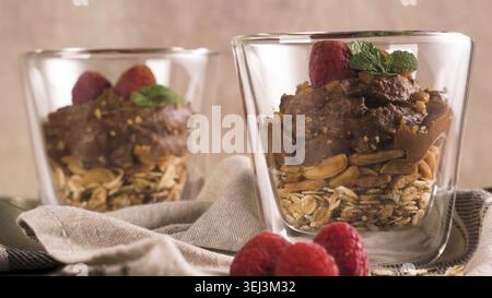 Couple of glasses of chocolate and chestnuts mousse with roasted almonds and oats decorated with raspberries and mint leaves Stock Photo