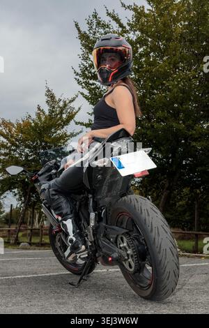Woman wearing a helmet and leather suit sitting on a black sports motorcycle Stock Photo