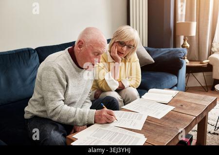 Senior, couple and writing documents in home for planning budget, retirement assets and sign legal contract for insurance policy. Man, woman and Stock Photo