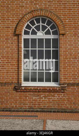 White painted wood arched window in a red brick wall Stock Photo