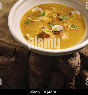 Food, A flavorful seafood stew is served in a rustic bowl, featuring clams, herbs, and lemon slices. The dish is set on a textured wooden table, creat Stock Photo