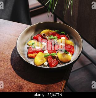 Food, A vibrant salad is presented in a round dish, showcasing yellow and red peppers, cheese, and fresh herbs. The dish is set on a wooden table, ill Stock Photo