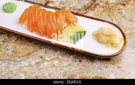 Food, Delicious slices of fresh salmon arranged neatly on a long white plate, accompanied by cucumber and a small mound of wasabi. The dish sits on a Stock Photo