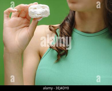 Food, A young woman holds a delicate sweet treat close to her mouth, looking pleased. She is dressed in a green top, with her hair styled in loose cur Stock Photo