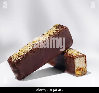 Food, Two chocolate-coated dessert bars sit on a light background, showcasing a smooth exterior topped with crushed nuts. The bars have a soft, creamy Stock Photo