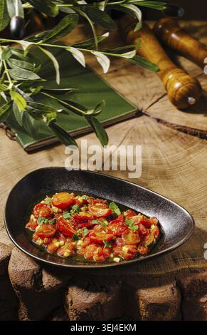 Food, Bright red tomatoes are arranged on a black plate, garnished with herbs. The rustic wooden background features natural textures and greenery, cr Stock Photo