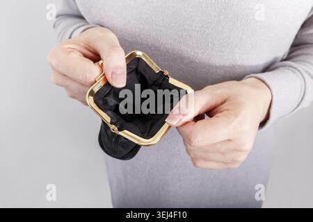 Woman holding open black empty wallet wearing gray clothes Stock Photo