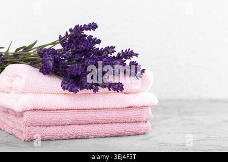 Stack of pink cotton towels and bouquet of lavender flowers on the grey stone trendy background, close up with coopy space Stock Photo