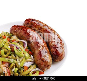 Food, Two golden-brown sausages lay on a white plate alongside a colorful mix of fresh vegetables like peppers and onions. The food looks appetizing a Stock Photo