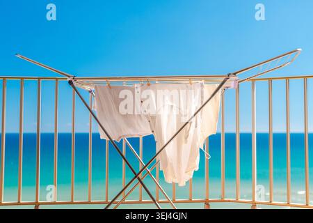 White summer clothes drying on balcony with turquoise ocean view during sunny tropical beach vacation Stock Photo
