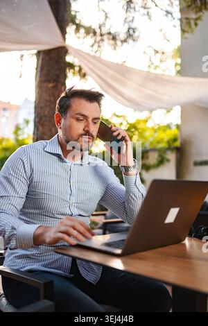Man working remotely outdoors using laptop and smartphone Stock Photo