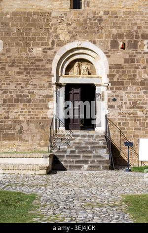 Vieste - Apulia - Italy - 08-29-2025: Stone facade with arched doorway and open wooden door, showing steps, metal railings, and a small information si Stock Photo
