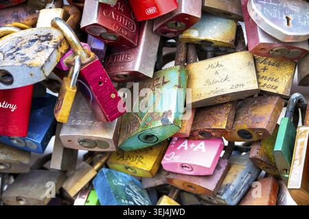 Koeln - North Rhine-Westphalia - Germany - 11-02-2024: Close view of assorted padlocks with paint, rust and engraved names hanging tightly together on Stock Photo