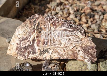 Large agate stone with natural lines in white, brown, and red, placed on stones, with sharp edges and organic inclusions Stock Photo