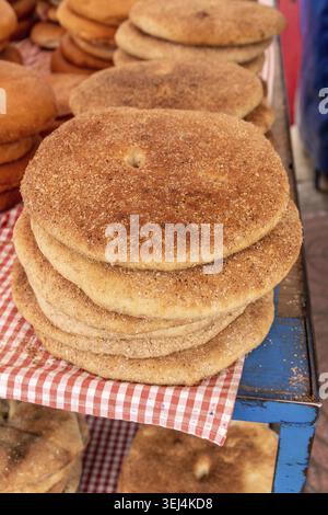 A stack of round, golden brown loaves rests on a red-and-white checkered cloth on a blue table, showing a uniform crust and slightly grainy texture Stock Photo