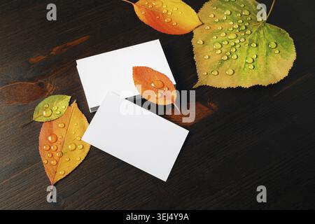Photo of blank business cards and autumn leaves with water droplets on wood table background Stock Photo