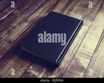 Photo of blank book with black hardcover on wood table background. Vintage toned image Stock Photo