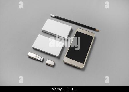 Gadgets and stationery. Mockup of blank business cards, pencil, usb flash drive and cellphone with blank screen on gray paper background Stock Photo