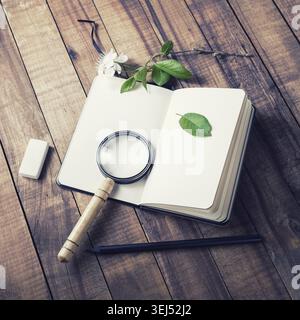 Photo of blank opened notebook, magnifier, pencil, eraser, cherry flowers and green leaves on vintage wood background. Stationery set for placing your Stock Photo