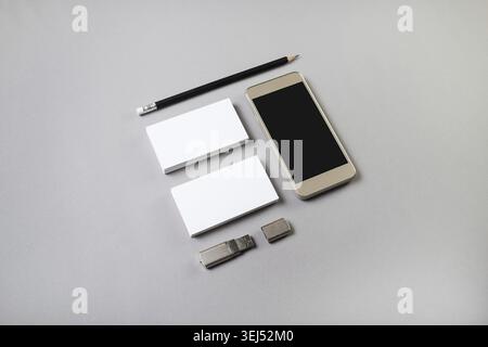 Photo of smartphone with blank screen, business cards, pencil and usb flash drive on gray background. Blank stationery template Stock Photo