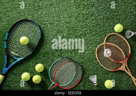 Tennis racket badminton rackets tennis balls and shuttlecocks arranged on green artificial grass sports background with copy space. Stock Photo