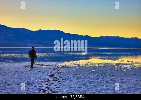 Hiker Walking at Sunrise on Salt Flats Reflections at Badwater Basin Death Valley Stock Photo