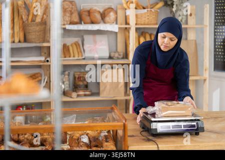 Middle-aged Muslim saleswoman weights cookies in bakery Stock Photo