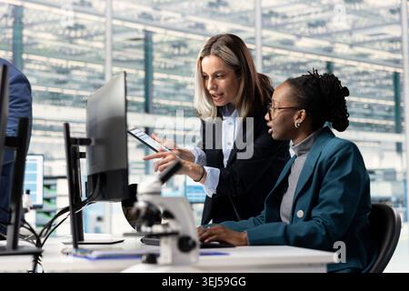 African american woman and coworker doing semiconductors hardware prototyping in office, brainstorming. Female engineering team collaborating on technical innovations in microchip factory RD lab Stock Photo