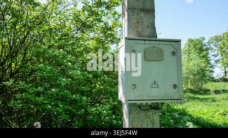 Electrical box on a concrete pole in a rural area with green trees Stock Photo