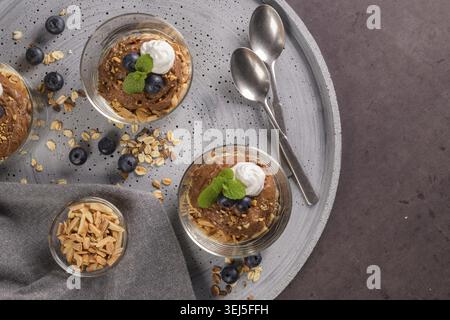 Glass cups of chocolate and chestnuts mousse with roasted almonds and oats decorated with black berries and mint leaves Stock Photo