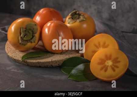 Ripe persimmon fruits in a cork plate on dark kitchen counter top Stock Photo