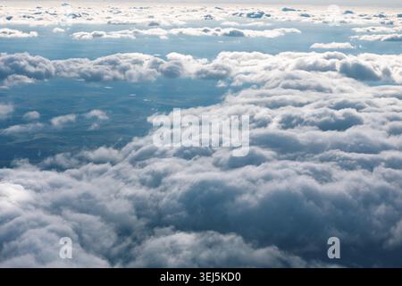 Aerial view of a landscape partially obscured by a dense layer of cumulus clouds. Puffy white clouds float gently across a brilliant blue sky Stock Photo