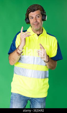 Adult man in reflective polo shirt listening to music and dancing on green screen Stock Photo